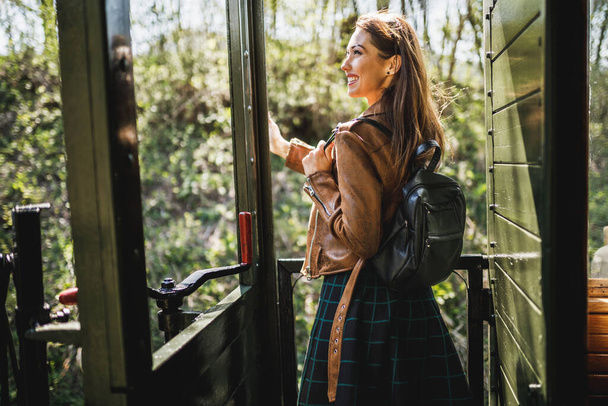 A smiling young woman with a backpack on her back traveling in an adventure by retro train. - Fotoğraf, Görsel