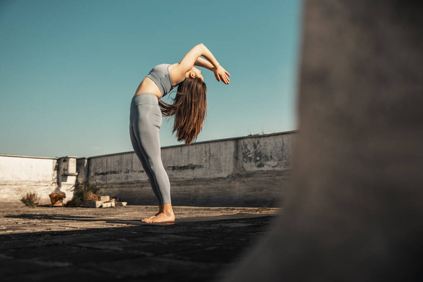 Relaxed young woman practicing yoga on a rooftop terrace. Sky in the background. - Foto, immagini