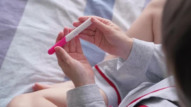 Happy woman lying in bed and making pregnancy test. Unrecognizable girl holding positive pregnancy test with two lines. Pregnancy concept, family planning. - Footage, Video