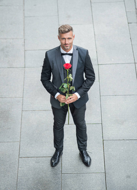 elegant man in tuxedo. man wearing bowtie suit outdoor. charismatic tuxedo man with red rose. - Foto, afbeelding