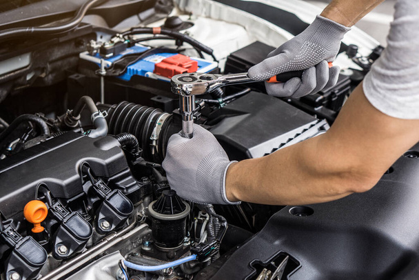 Mechanic man working on the engine of the car in the garage.Car service and maintenance,Repair service.Checks car engine under the hood - 写真・画像
