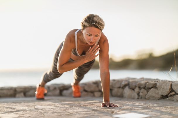 S'adapter femme d'âge moyen faisant des exercices de planche ou push-up pendant l'entraînement dur près de la plage de la mer. - Photo, image