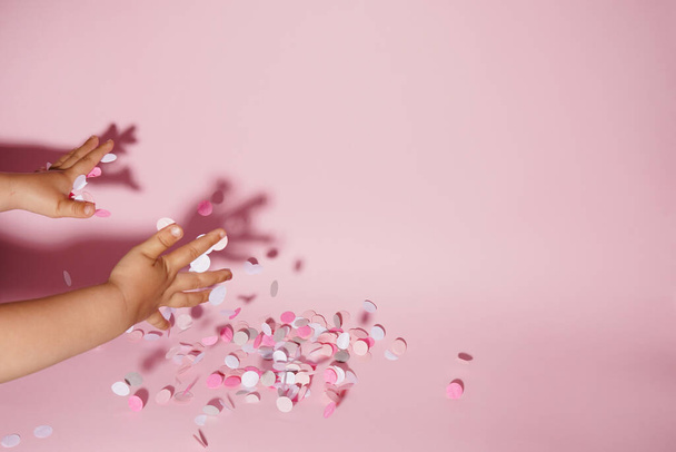Falling confetti in child hands on bright pink background, copy space - Fotoğraf, Görsel