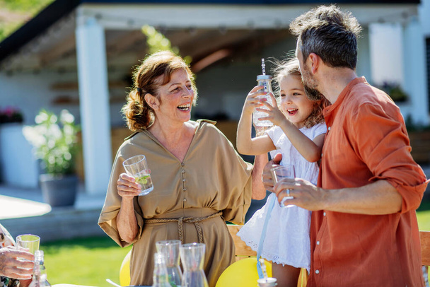 Multi generation family having garden party celebration, little girl with her dad and grandmother drinking a water with lemon, having nice time. - Foto, Imagen