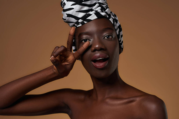 Elegant black girl wearing traditional african turban showing victory sign and looking at camera. Beautiful young slim woman. Female beauty. Isolated on orange background. Studio shoot. Copy space - Photo, Image
