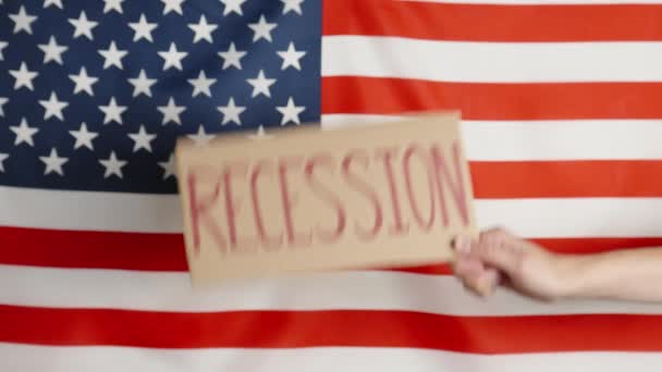Concept of economic crisis, recession and inflation in USA, Woman hand show cardboard sheet with word recession against american flag, Rising prices for consumer goods and services - Кадры, видео