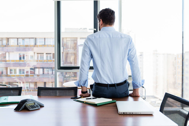 Shot of a businessman sitting with his back on office desk and looking out the window. - Foto, Imagen
