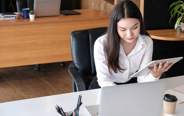 Junge asiatische Geschäftsfrau arbeitet im Büro am Tablet mit Laptop - Foto, Bild