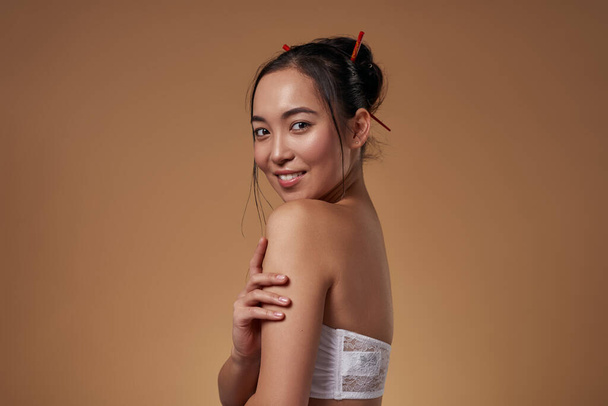 Side view of smiling stylish asian girl looking at camera. Attractive young brunette slim woman wearing tank top. Female beauty. Isolated on orange background. Studio shoot. Copy space - Φωτογραφία, εικόνα