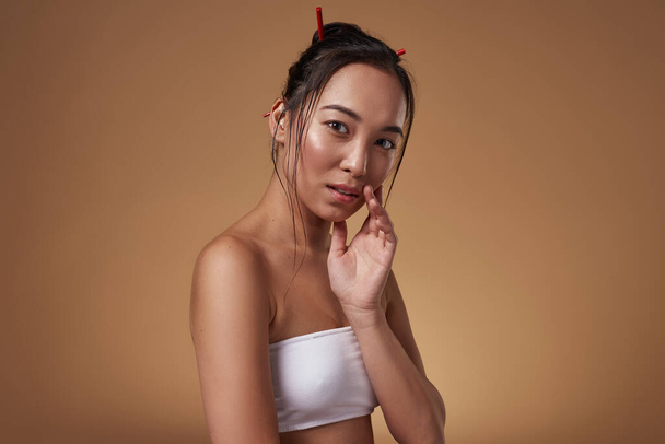 Serious stylish chinese or korean girl looking at camera. Attractive young brunette slim woman wearing tank top. Female beauty. Isolated on orange background. Studio shoot. Copy space - Foto, imagen