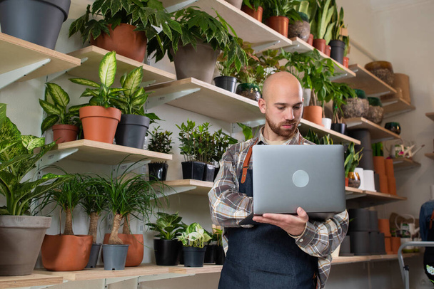 Caucasian entrepreneur man in the floral store using the laptop to checking the inventory of shop then looking to the camera smiling large. - Foto, imagen