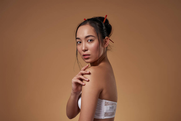 Side view of serious elegant asian girl looking at camera. Beautiful young brunette slim woman wearing tank top. Female beauty. Isolated on orange background. Studio shoot. Copy space - Fotoğraf, Görsel