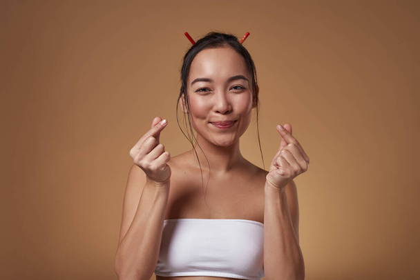 Smiling stylish asian girl with cross fingers looking at camera. Attractive young brunette slim woman wearing tank top. Female beauty. Isolated on orange background. Studio shoot. Copy space - Photo, Image