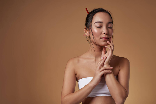 Partial image of fashionable asian girl with closed eyes. Pretty young brunette slim woman wearing tank top. Female beauty. Isolated on orange background. Studio shoot. Copy space - Φωτογραφία, εικόνα