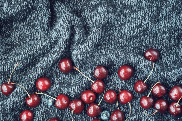 Red ripe cherries scattered on a dark blue knitted blanket. View from above. - Foto, Imagem