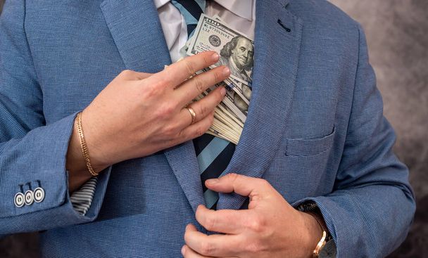 wysokiej rangi urzędnik w eleganckim drogim garniturze wkłada skradzione pieniądze do kieszeni. Koncepcja przekupstwa - Zdjęcie, obraz