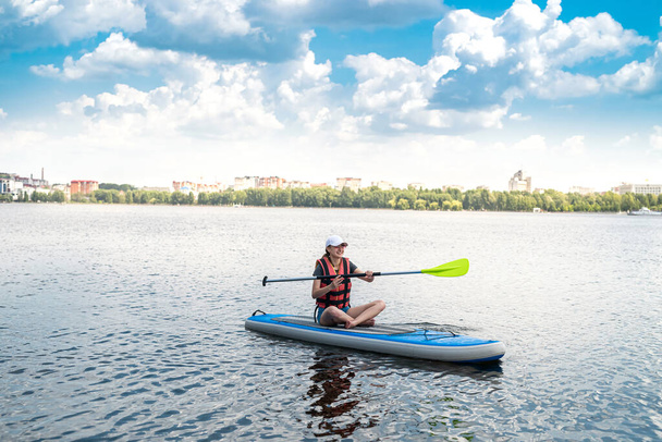 Charming smiling woman rides a sup paddle board around city lake, active lifestyle, sport and health - Photo, Image