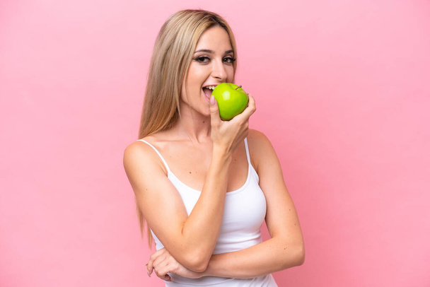 Pretty blonde woman isolated on pink background eating an apple - Foto, Bild