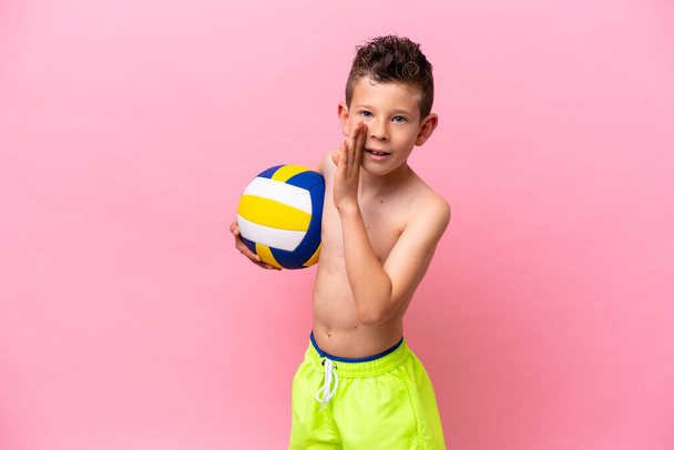 Little caucasian boy playing volleyball isolated on pink background whispering something - Фото, изображение