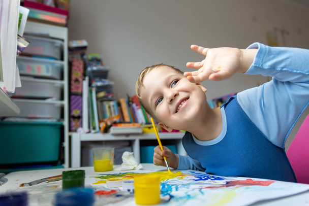 Portrait of cute little blond kid boy enjoy have fun painting with watercolor and brush bright abstract inage on paper at home or kindergarten class. Imagination development children play activity. - Photo, image