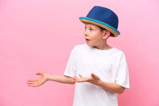 Pequeño chico caucásico con un sombrero aislado sobre fondo rosa con expresión facial sorpresa - Foto, imagen