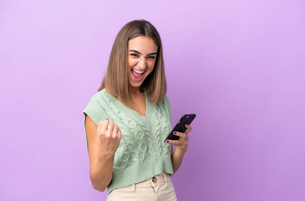 Young caucasian woman isolated on purple background with phone in victory position - Photo, Image