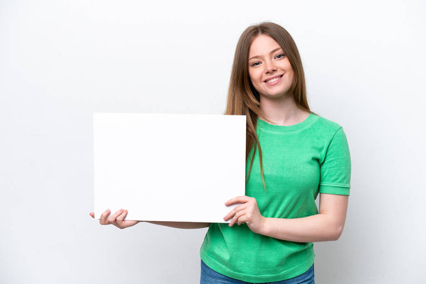 Young caucasian woman isolated on white background holding an empty placard with happy expression - 写真・画像