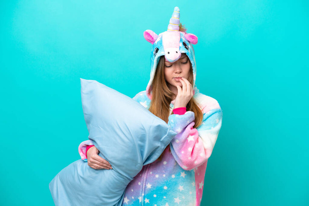 Young caucasian girl with unicorn pajamas holding pillow isolated on blue background having doubts - Foto, imagen