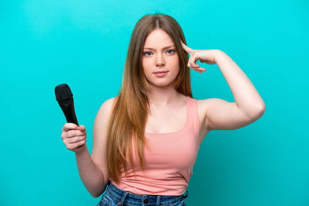 Singer caucasian woman picking up a microphone isolated on blue background having doubts and thinking - Foto, Bild