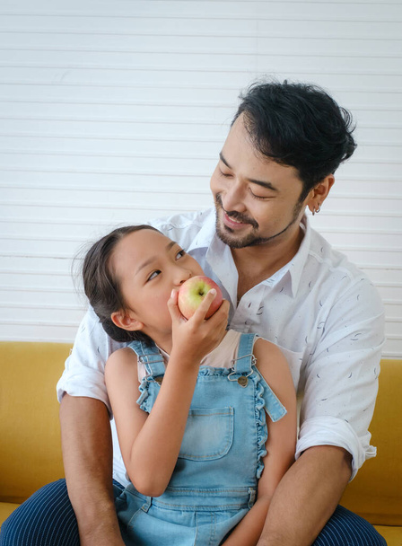 Asian happy family. Father looking his daughter eating apple and very happy. - Fotoğraf, Görsel