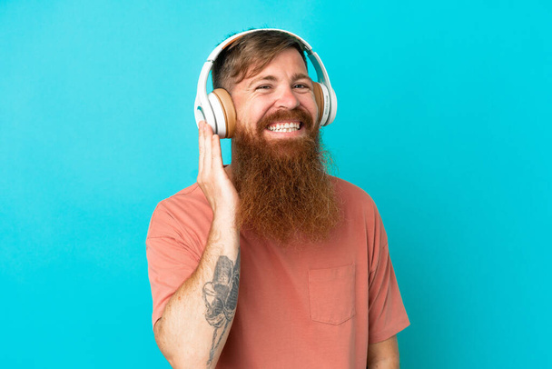 Jovem caucasiano avermelhado homem isolado no fundo azul ouvir música - Foto, Imagem