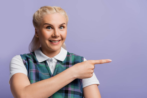 Cheerful student in vest and shirt pointing with finger isolated on purple  - Foto, imagen