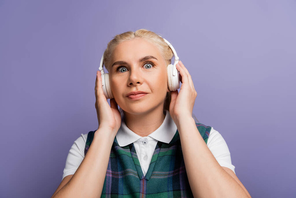 Blonde student in checkered vest using headphones isolated on purple  - Photo, Image