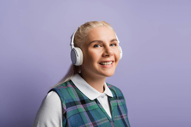Portrait of cheerful student in headphones looking at camera isolated on purple  - Fotografie, Obrázek