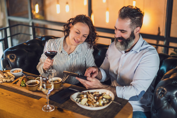 Ein erwachsenes Paar sitzt im Restaurant. Sie essen mit Wein zu Abend und verbringen schöne Zeit miteinander. - Foto, Bild