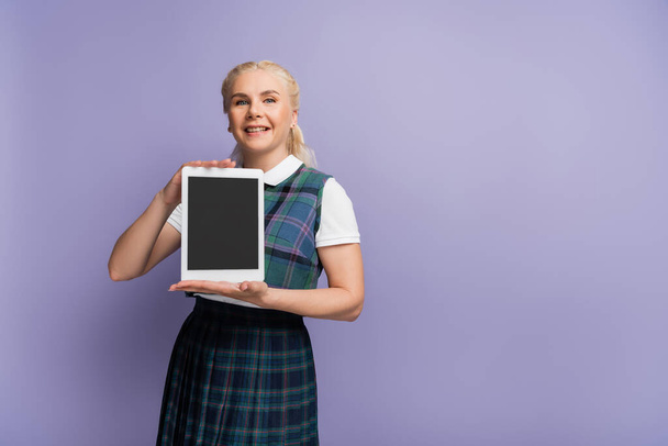 Cheerful blonde student holding digital tablet with blank screen isolated on purple  - Foto, imagen