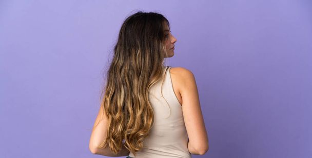 Jeune femme caucasienne isolée sur fond violet en position arrière et regardant côté
 - Photo, image