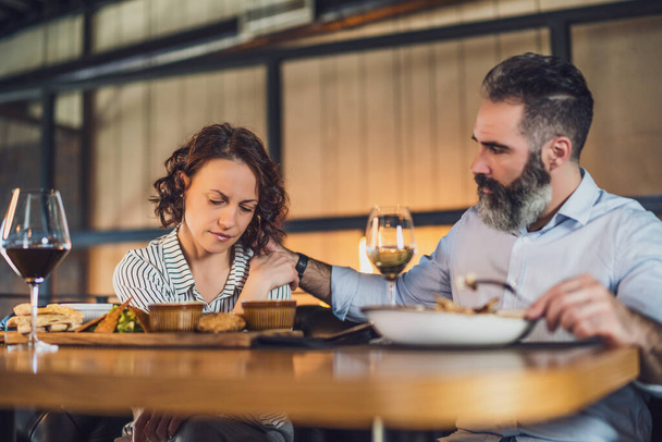 Ein erwachsenes Paar sitzt im Restaurant. Sie essen mit Wein zu Abend. Frau ist traurig und deprimiert. - Foto, Bild