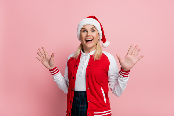 Excited woman in santa hat looking at camera isolated on pink  - Zdjęcie, obraz