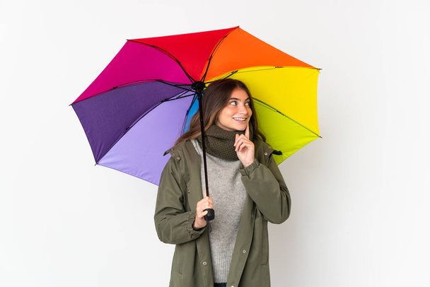 Young caucasian woman holding an umbrella isolated on white background thinking an idea while looking up - Fotografie, Obrázek