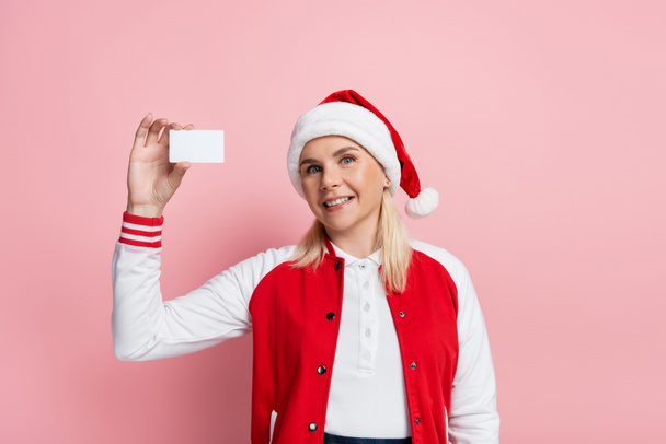 Blonde woman in red santa hat holding driving license with copy space isolated on pink  - Zdjęcie, obraz