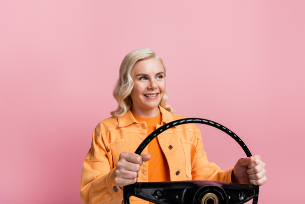 Blonde woman holding steering wheel and looking away isolated on pink  - Foto, immagini
