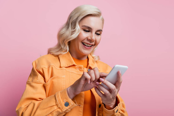 Pretty blonde woman using smartphone isolated on pink  - Фото, изображение