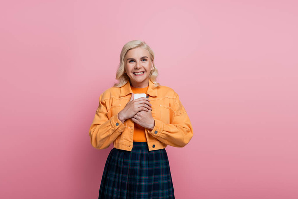Happy blonde woman holding smartphone and looking at camera isolated on pink  - Valokuva, kuva