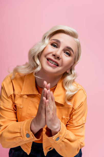 Blonde woman showing praying hands at camera isolated on pink  - Foto, imagen