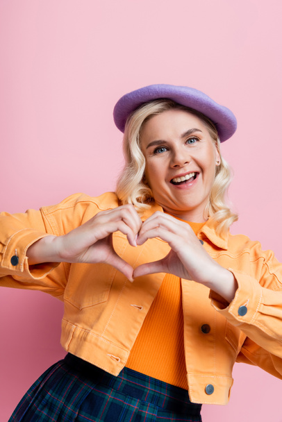 Positive blonde woman in beret showing heart sign isolated on pink  - Foto, afbeelding
