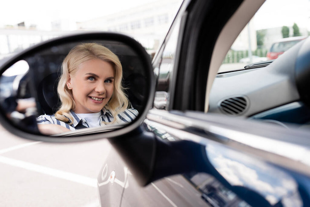 Positive woman reflecting in blurred car mirror  - Foto, Imagen