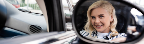 Cheerful blonde woman reflecting in blurred mirror of auto, banner  - Fotó, kép