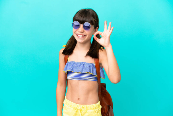 Klein blank kind gaat naar het strand geïsoleerd op blauwe achtergrond met ok teken met vingers - Foto, afbeelding