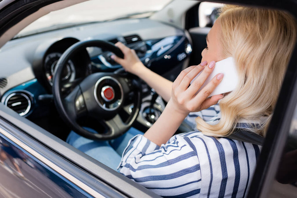 Blonde woman talking on smartphone while driving blurred car  - Foto, imagen